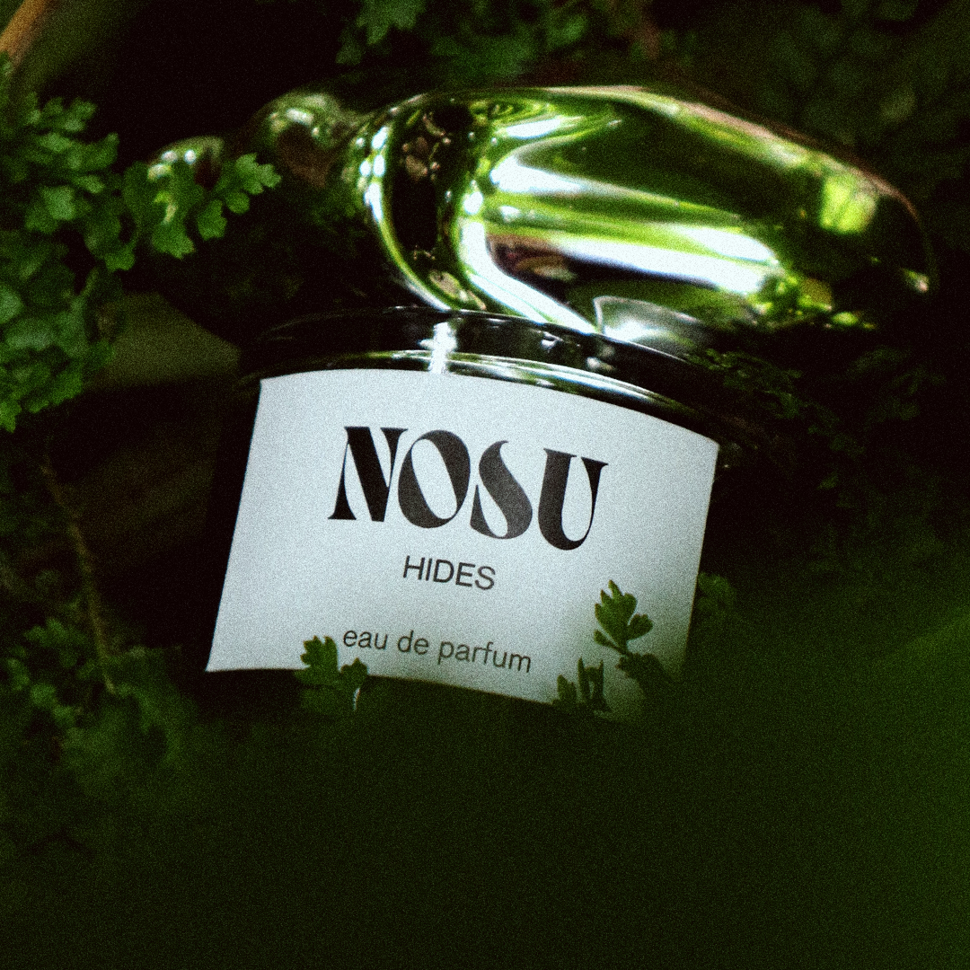 Perfume with 'NOSU' label in a natural setting of leaves